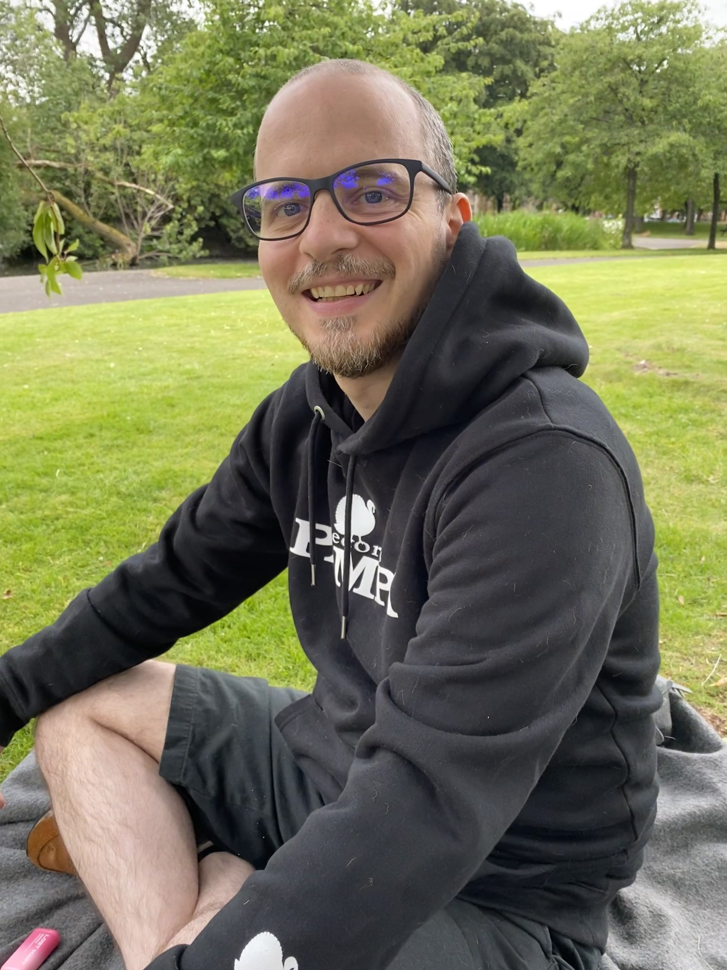 a man with glasses sitting and smiling in the park